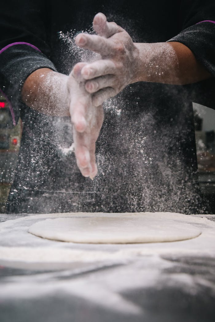 services-04 A chef clapping hands over dough, releasing flour in a kitchen setting.